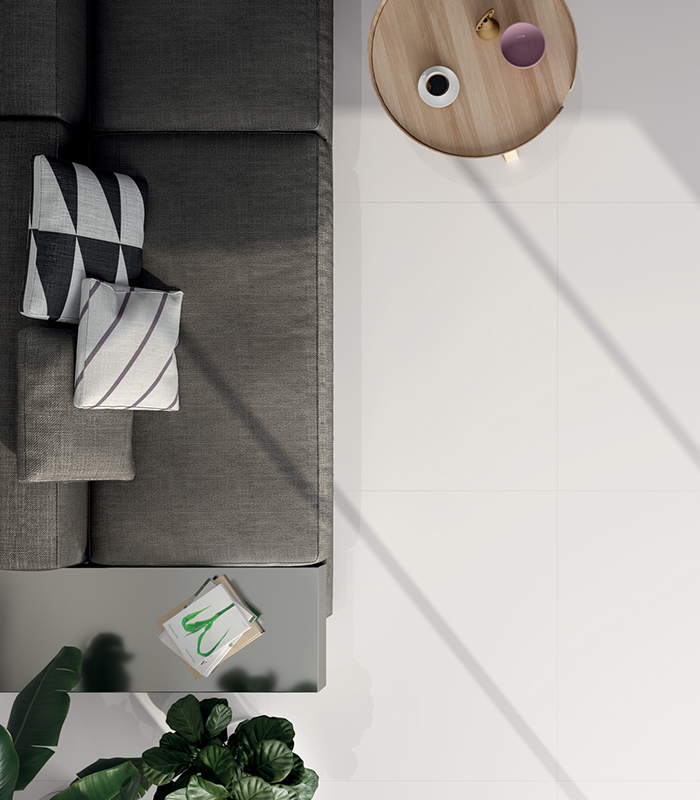 Top view of a modern living room with a grey sofa, a round coffee table in light wood, and a glossy white marble-effect floor.