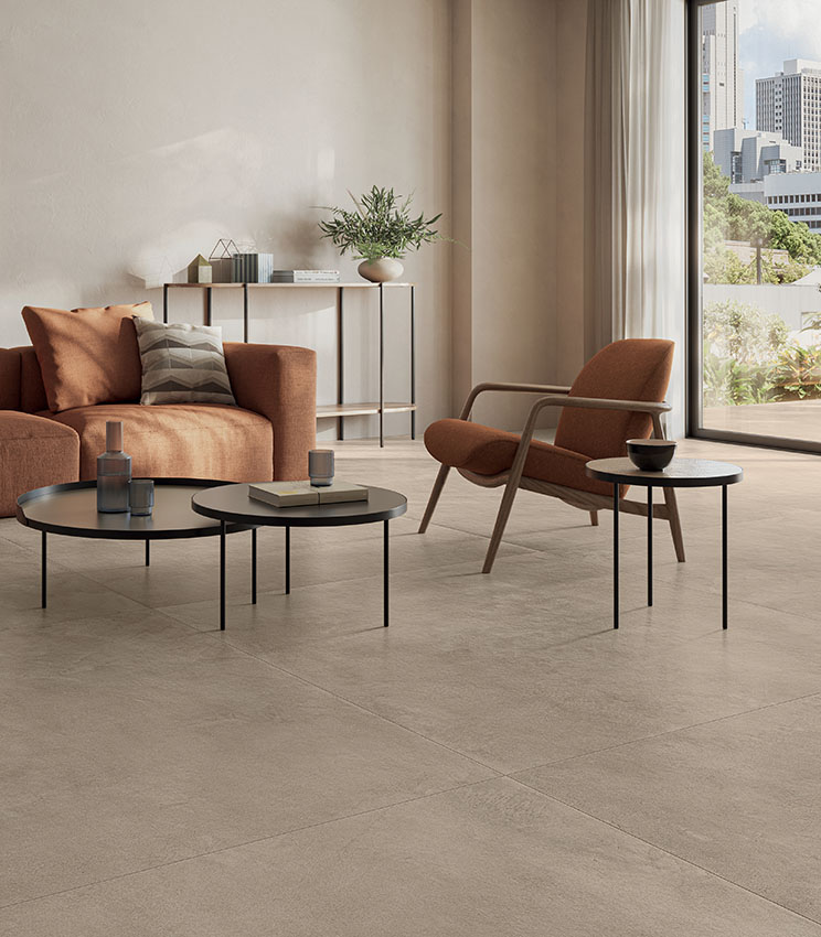 Modern living room with warm, earthy tones, featuring French doors opening onto a terrace and sand-colored concrete-effect porcelain stoneware flooring.