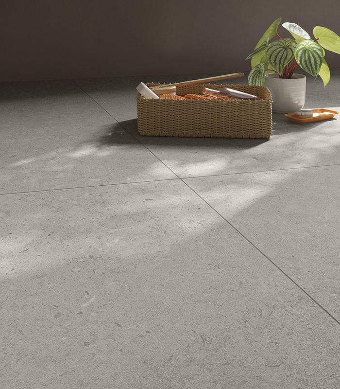 Close-up of light-colored stone-effect porcelain stoneware flooring, with a small bathroom accessories container and a potted green plant.
