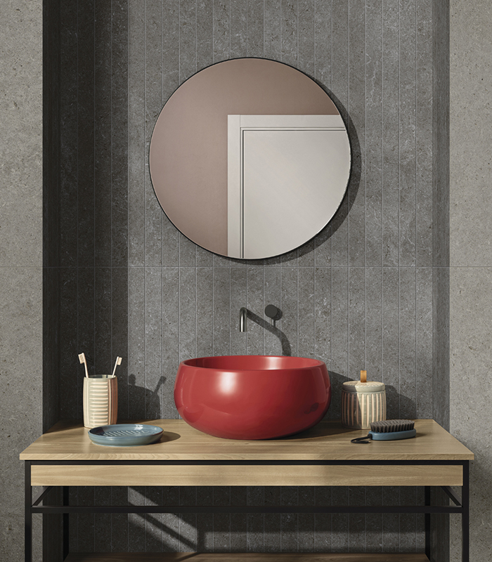 Front view of a washbasin area with stone-effect porcelain stoneware strips, round mirror, and red countertop sink.          Chiedi a ChatGPT