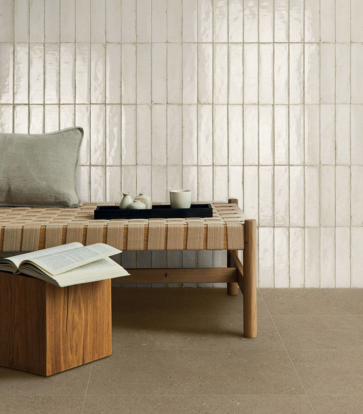 Modern and relaxing interior with a wooden bench and woven seat, a wall clad in glossy ivory ceramic tiles and porcelain stoneware flooring in natural tones.