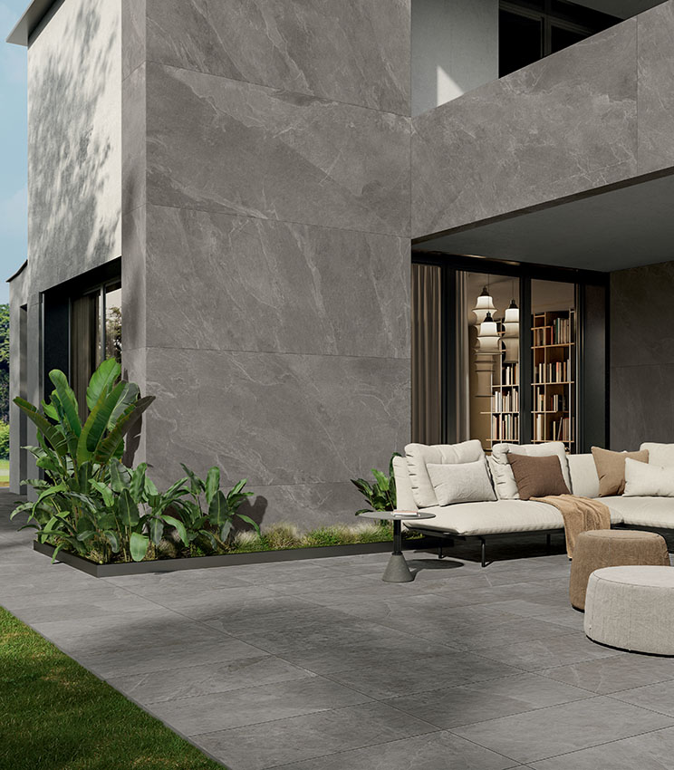 External view of a modern villa with rigorously geometric design, partially clad in large stone-effect ceramic slabs, featuring a furnished patio paved with 20-mm-thick stone-effect porcelain stoneware.