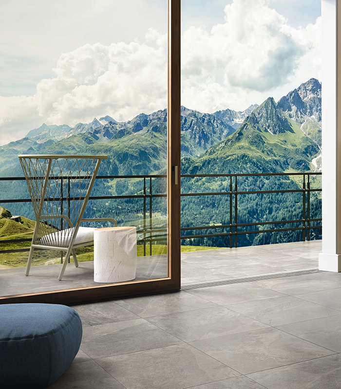 View of the floor of the outdoor paving and French window of a bedroom. Matching outdoor and indoor flooring in gray stone-effect porcelain stoneware.