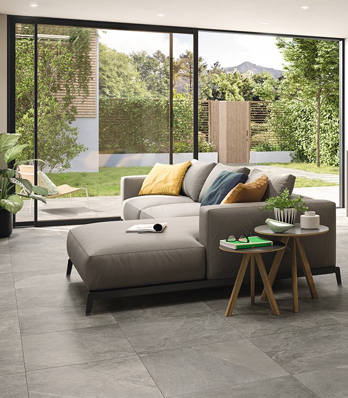 View of open-plan living room and kitchen with large glass door overlooking a small private garden. Grey stone-effect porcelain stoneware flooring.