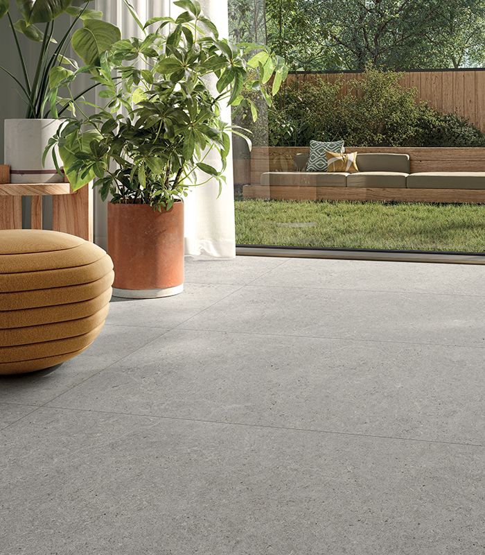 Zona living con vista sul giardino e pavimento in gres chiaro Surround di Panaria Ceramica, per una continuità tra interno ed esterno.