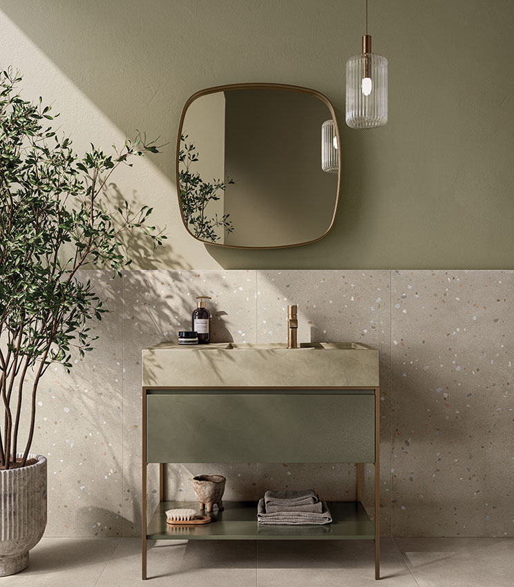 Contemporary bathroom featuring surfaces from the Formula Form Rope and Seed Rope collections, with a light wall covering accented by small coloured details, sage green walls, a matching vanity, a large shaped mirror, a pendant lamp and a decorative plant.