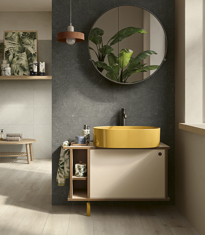 Small home bathroom with light wood-effect porcelain stoneware flooring and dark stone-effect ceramic wall tiles, featuring a yellow ceramic washbasin and a round mirror.