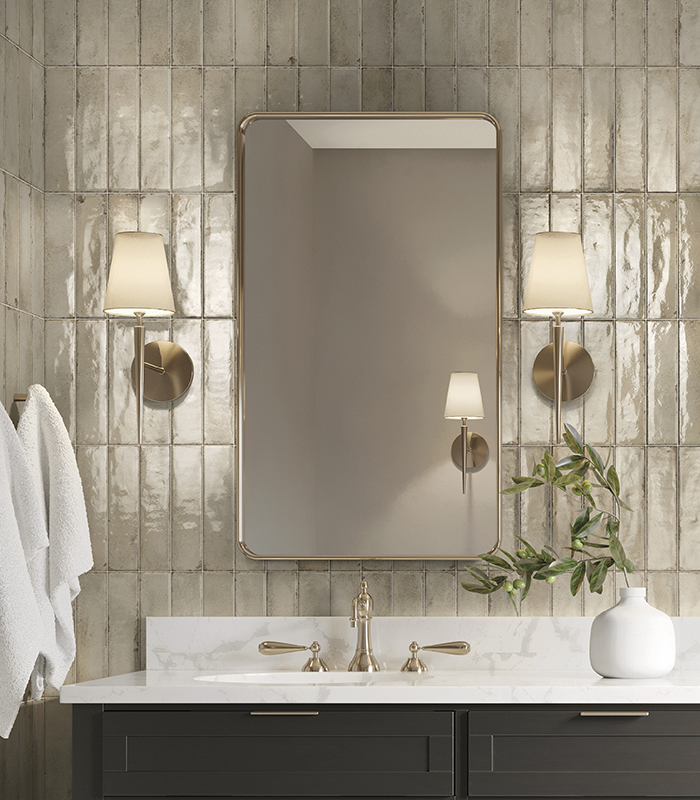 Detail of the washbasin wall in a small bathroom with ash-coloured wood-effect porcelain stoneware, featuring an oval mirror, a suspended light bulb, and tiles with a decorative brass insert.