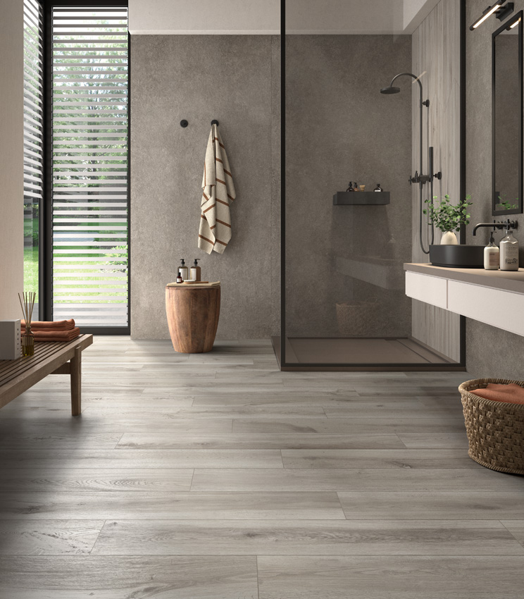 Modern bathroom with a glazed corner on the left and a washbasin on the right, a front-facing shower clad in grey stone-effect porcelain stoneware and a floor in grey ceramic wood-effect planks.