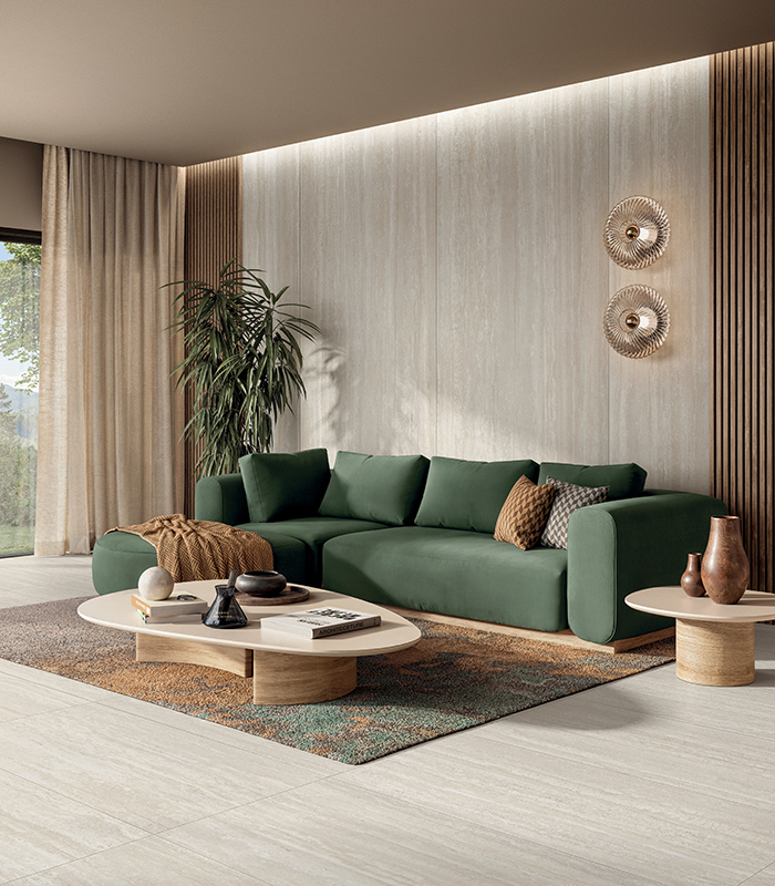 Scorcio di soggiorno elegante e moderno, dai toni neutri con un divano verde scuro, un tavolino da caffè, un tappeto dalle tonalità naturali e pavimento e rivestimento in gres effetto travertino.