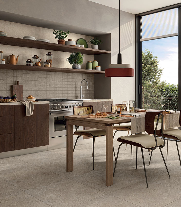 Modern kitchen with beige stone-effect floor and wall tiles, wooden furnishings, dining table and large window.
