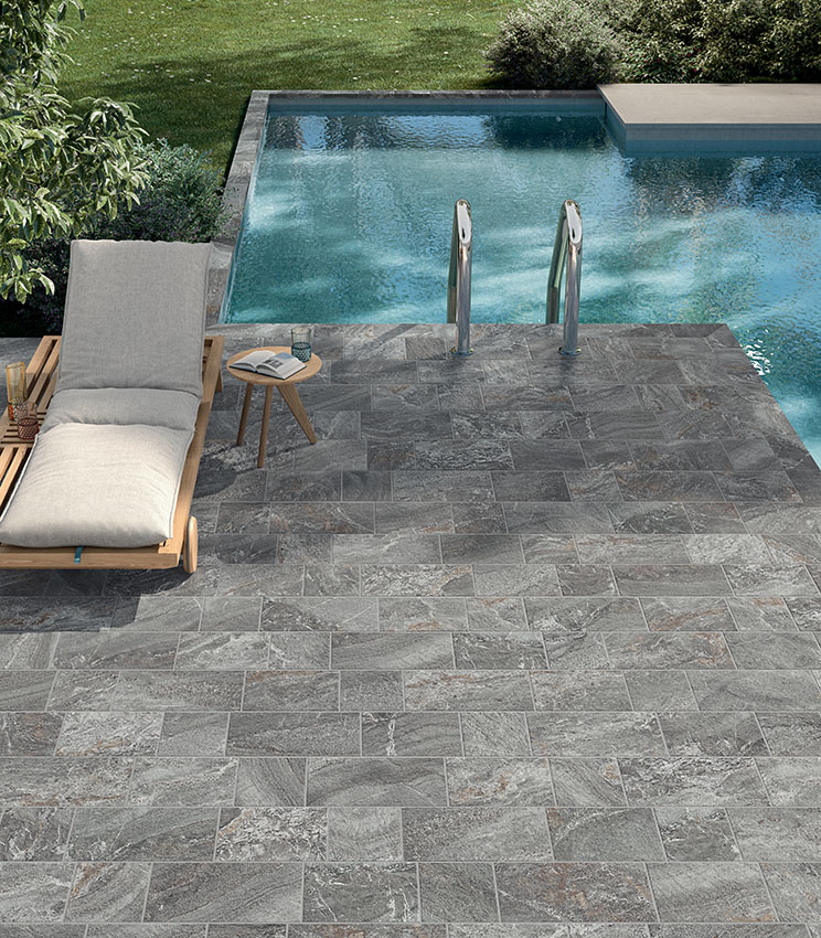 Poolside area with grey stone-effect porcelain stoneware flooring, sun lounger and pool ladder, creating an elegant, natural-looking and durable space.